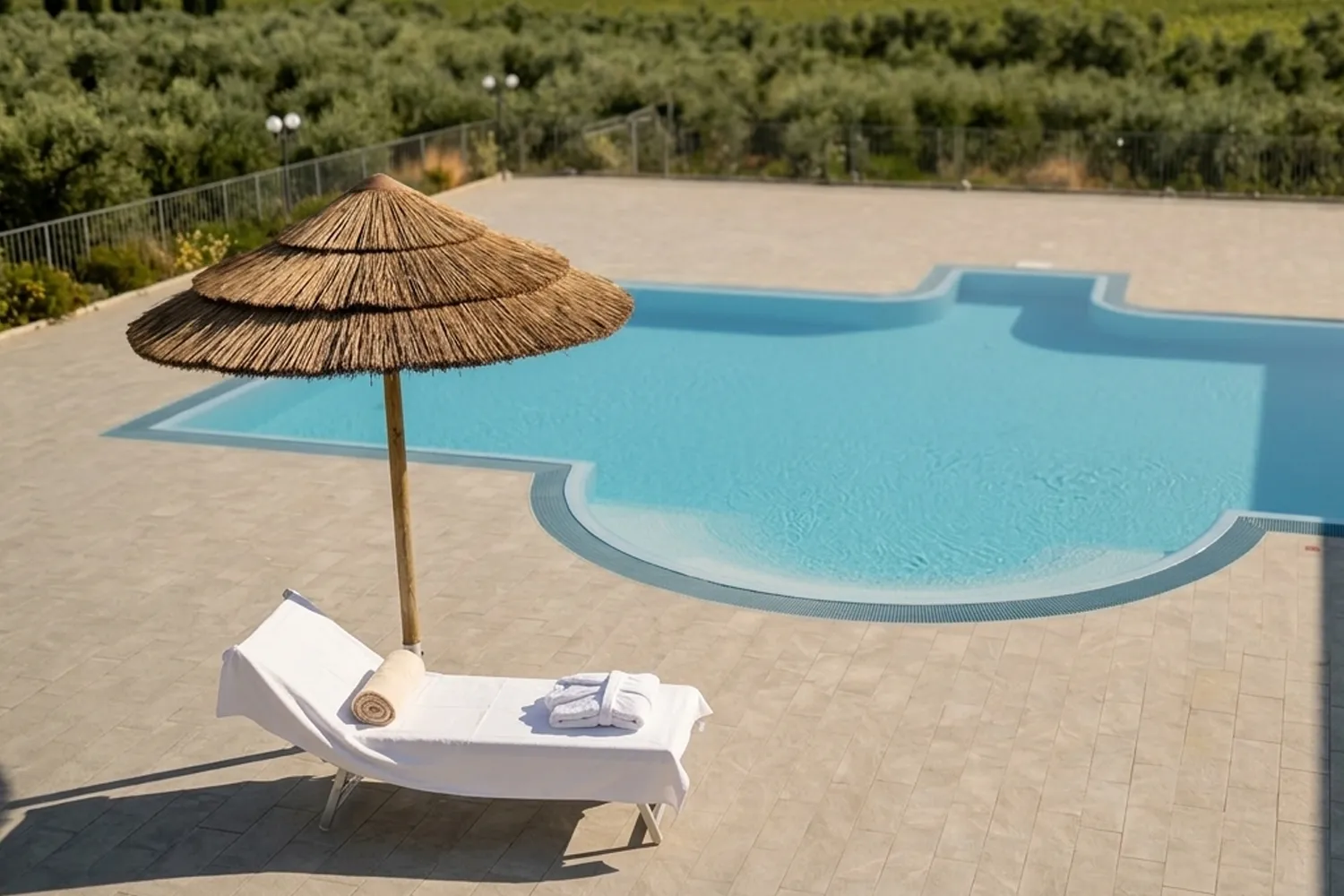 Lettino in lino bianco con asciugamano e accappatoio sotto ombrellone in paglia a bordo piscina per il pacchetto Relax d'Estate della Tenuta Elisabetta in Maremma.